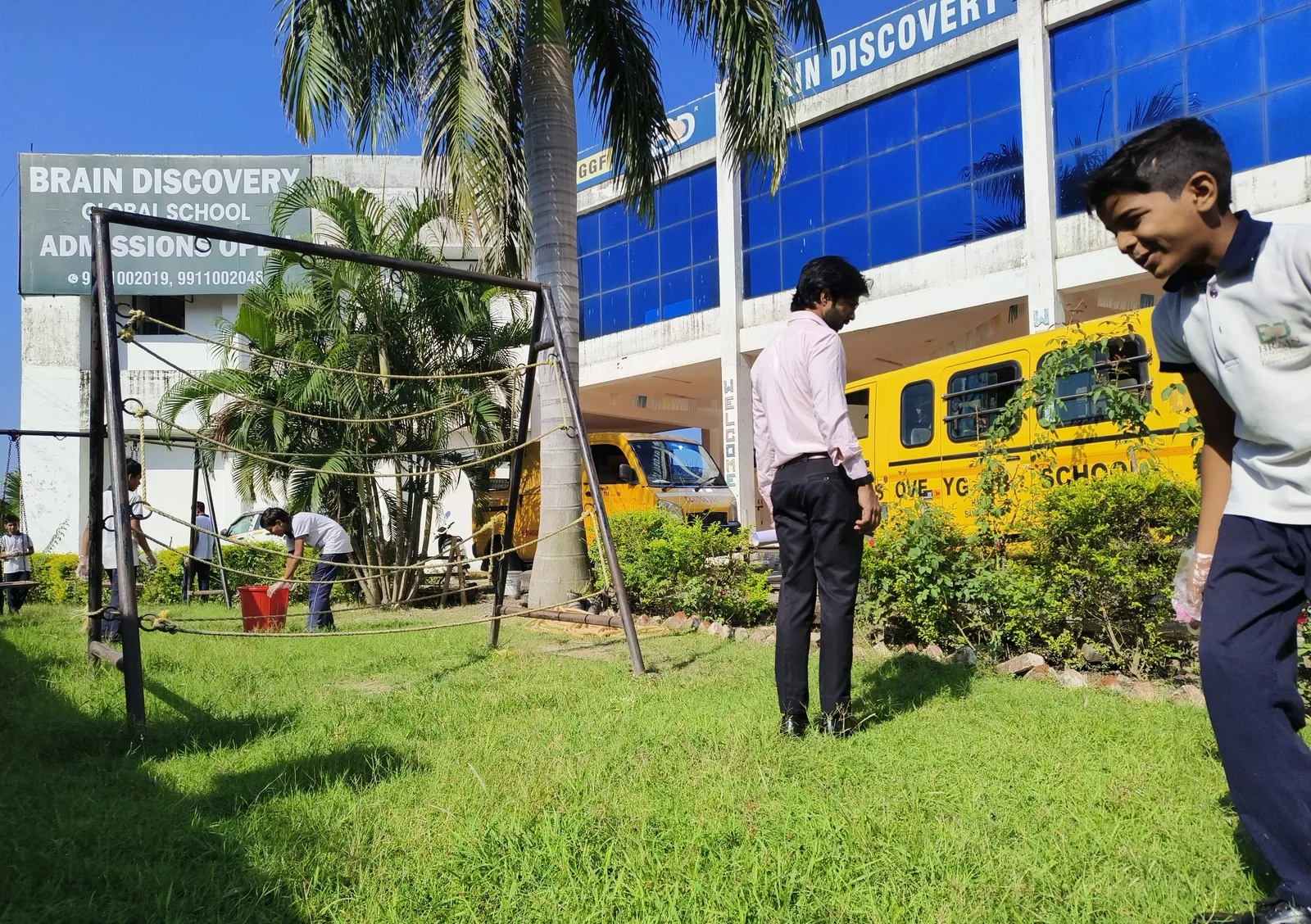 Students and teachers clearing the front garden, school buses parked behind them