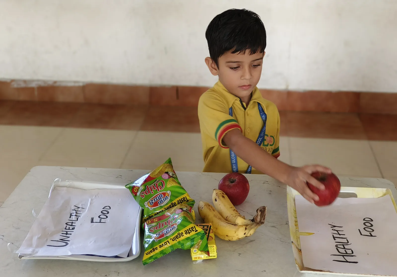 A boy puts an apple in the Healthy Food tray, the chips beside the Unhealthy Food tray