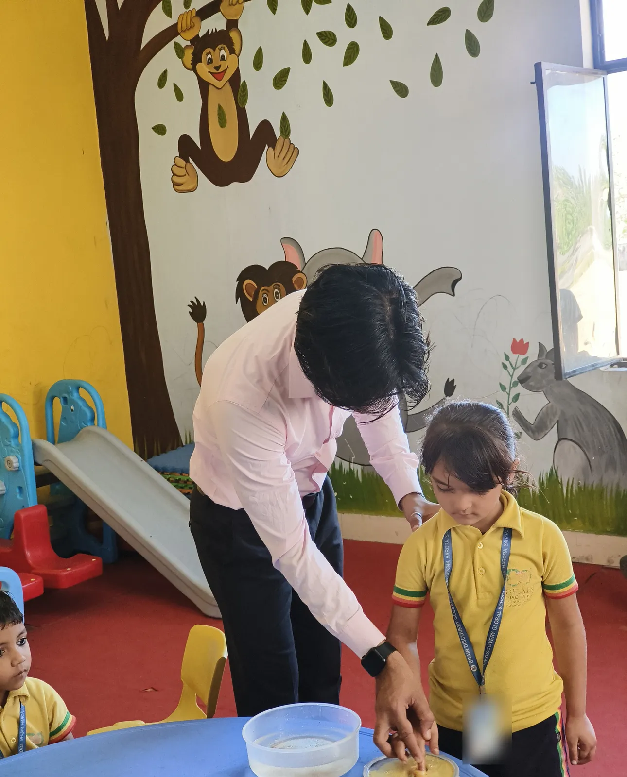 A girl watches as the teacher guides her finger into the dish of soap