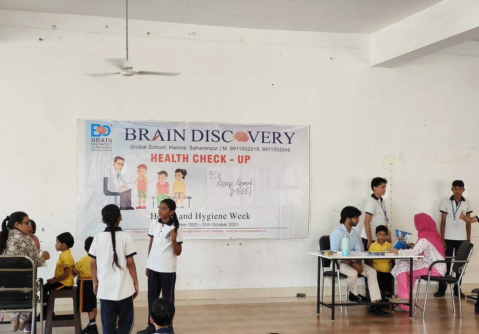 The school hall under a Health Check-up banner for Health and Hygiene Week, students at the check-up tables
