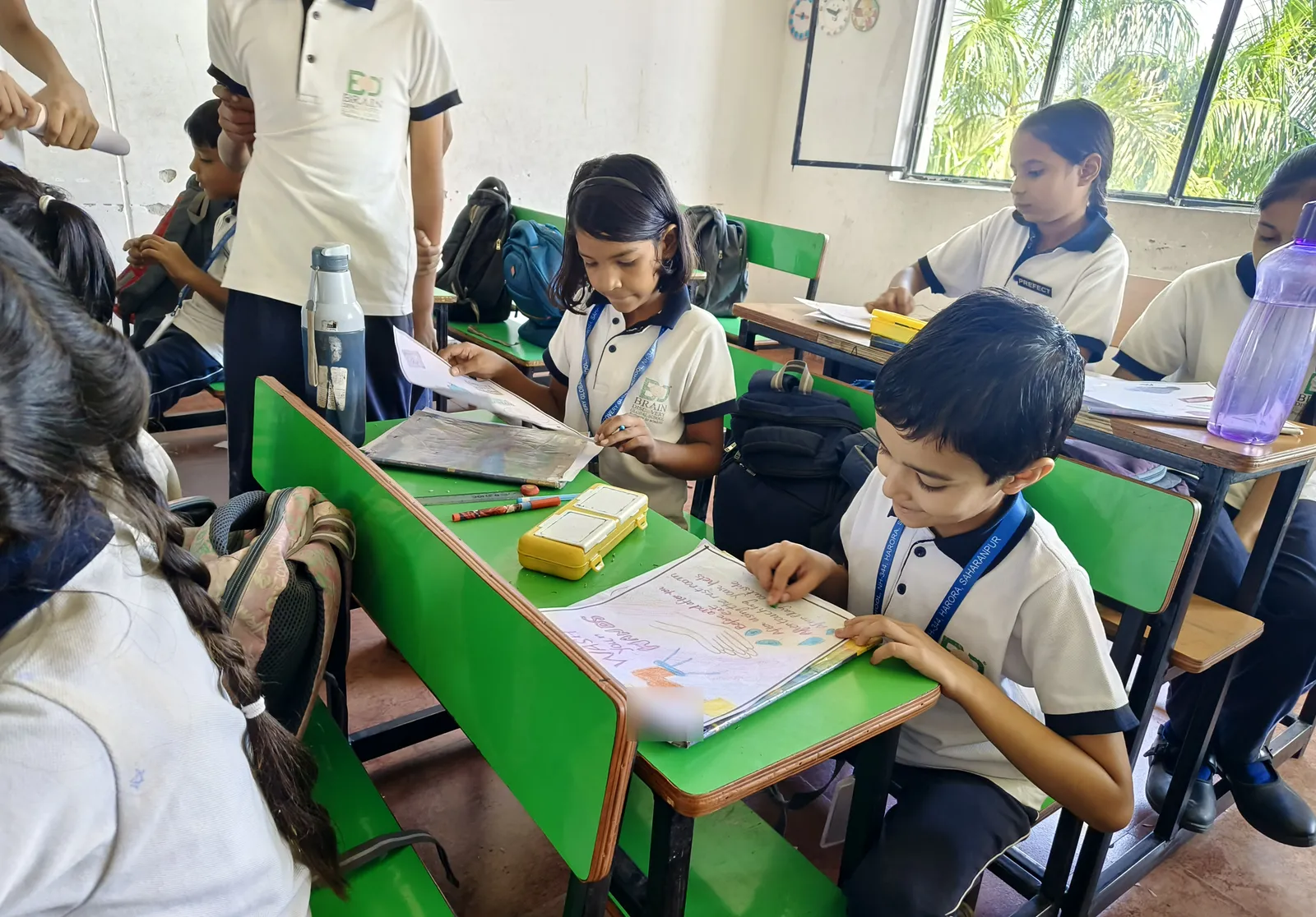 A classroom of older students colouring their posters, a boy smiling over his Wash Your Hands drawing