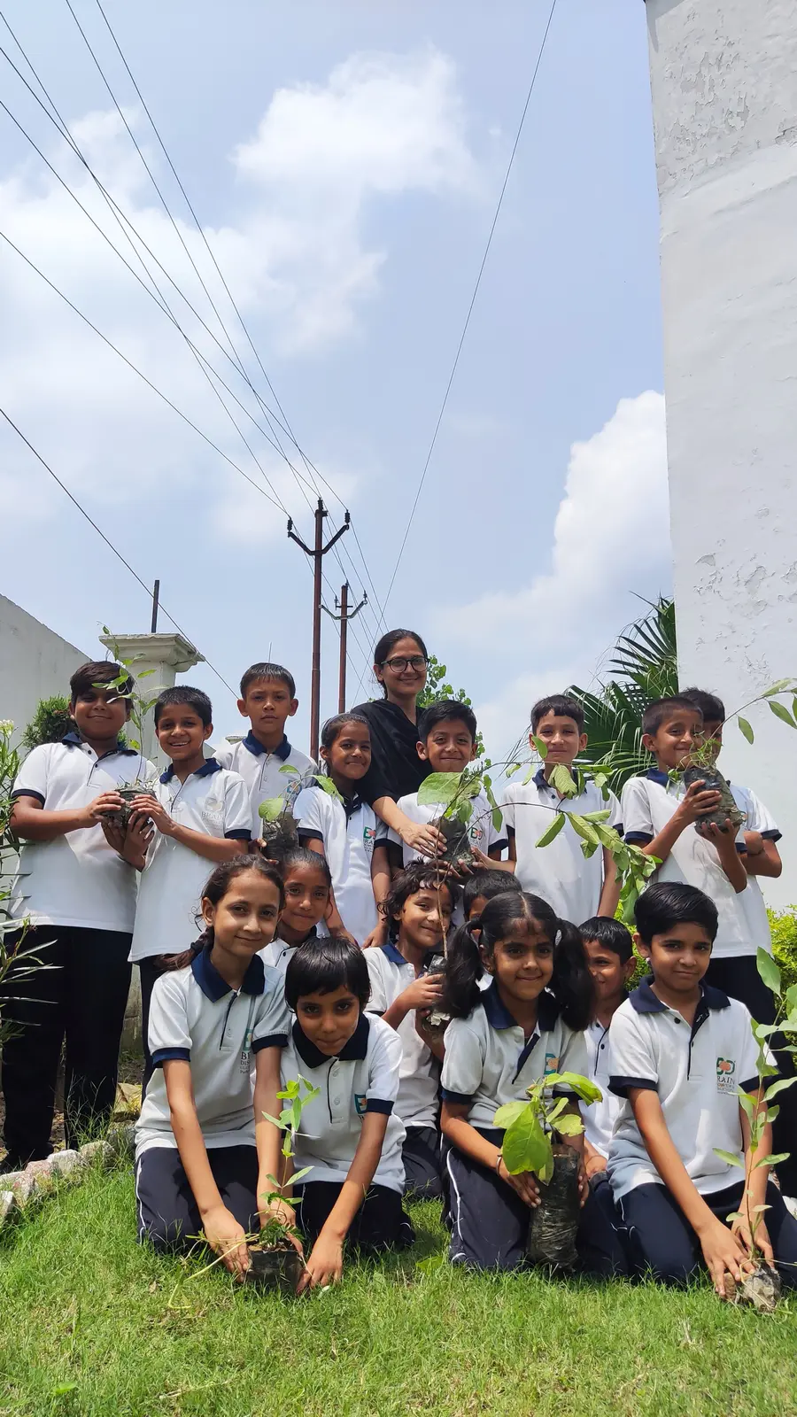 Students and a teacher holding saplings in the garden beside the school building