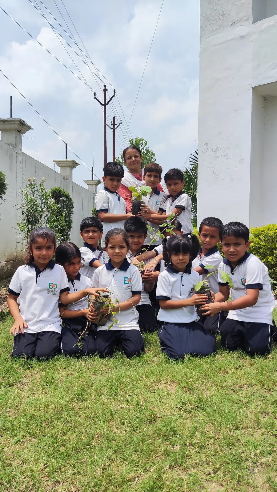 Young students kneeling with saplings in the garden with a senior teacher