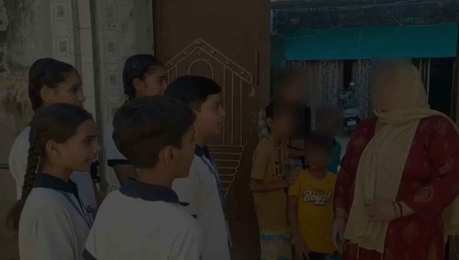 Students at a doorway talking to a woman as children look on