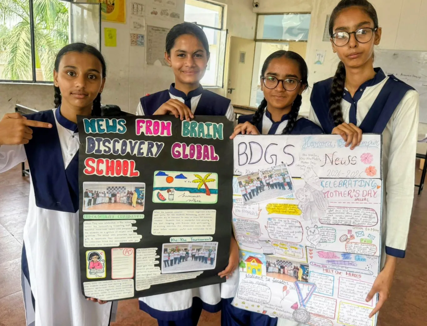 Four students hold up their hand-made school newspapers with stories on Mother’s Day, Labour Day and a kho-kho match