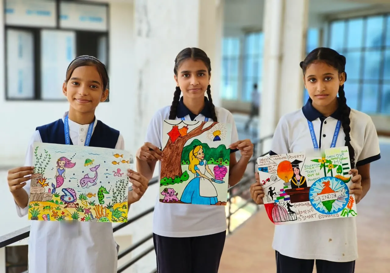 Three students holding up their drawings: an underwater scene, Alice in Wonderland, and a poster about education, women’s empowerment and a greener India